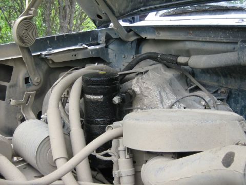 1995 Ford Bronco - The engine bay of a vehicle is shown with various hoses and a black cylinder visible.