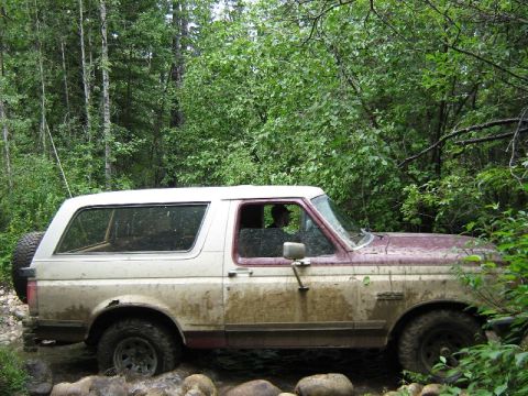 1995 Ford Bronco - This 1995 Ford Bronco navigates a challenging off-road path through a wooded area, with mud splattered on its body.