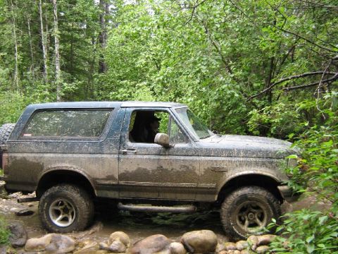 1995 Ford Bronco - Muddy 1995 Ford Bronco navigates a water crossing on a wooded trail.