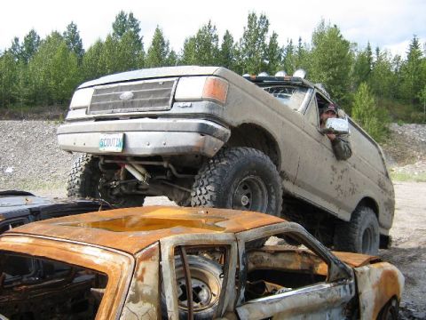 1995 Ford Bronco - This lifted 1995 Ford Bronco is shown driving over a wrecked vehicle in an outdoor setting.