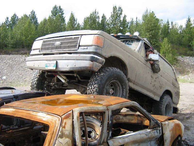 1995 Ford Bronco with lifted suspension and off-road tires driving over a rusted-out car