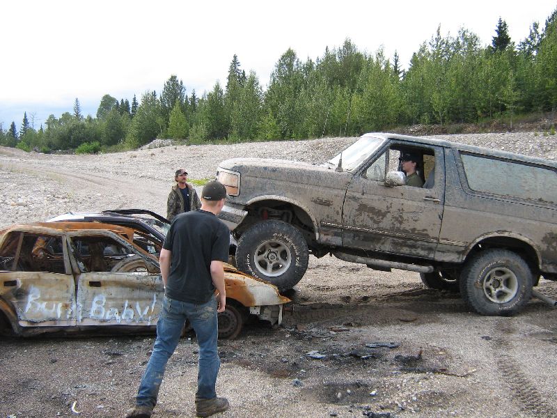 Muddy SUV on top of a burnt-out car. Two guys standing around