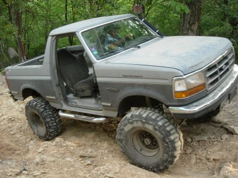 1995 Ford Bronco - Modified 1995 Ford Bronco tackling rough terrain with its large tires and open door.