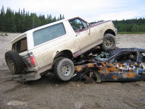 1995 Ford Bronco - A Ford Bronco is perched atop a destroyed vehicle in a dirt lot.