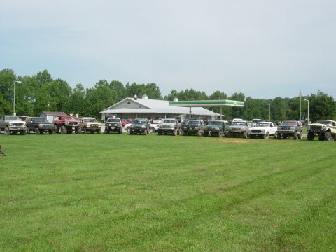 1995 Ford Bronco - A group of SUVs are parked in a field near a gas station under a bright sky.
