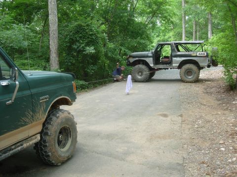 1995 Ford Bronco - Two off-road vehicles are connected by a tow rope on a dirt path in a wooded area.