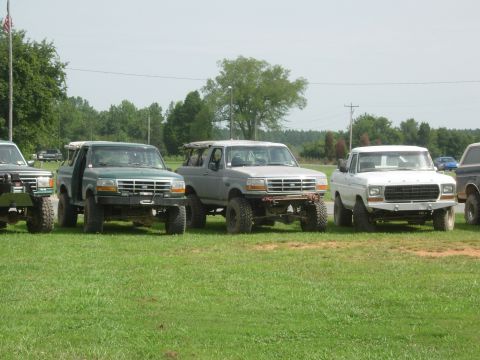 1995 Ford Bronco - A lineup of SUVs and a pickup truck are parked on a grassy field under a clear sky.