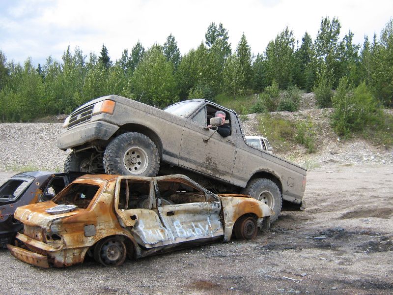 Ford pickup truck is parked on top of two wrecked cars in a dirt lot