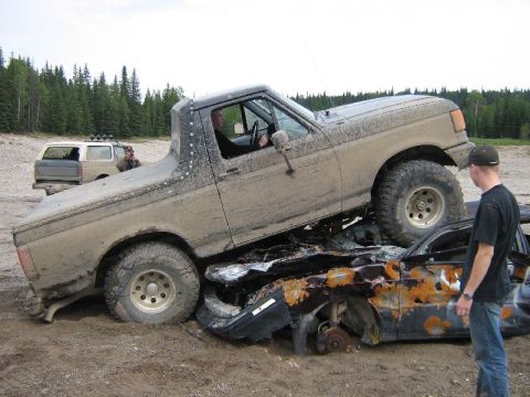 1995 Ford Bronco - A muddy Ford F-150 is driven over a destroyed car, with another SUV in the background.
