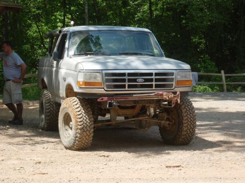 1995 Ford Bronco - A lifted 1995 Ford Bronco sits parked on a dirt path, ready for off-road adventure.