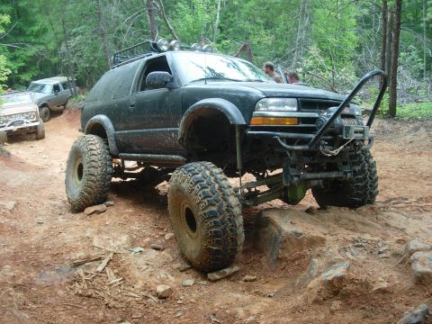 1995 Ford Bronco - Several off-road vehicles navigate a challenging dirt trail in a wooded area.
