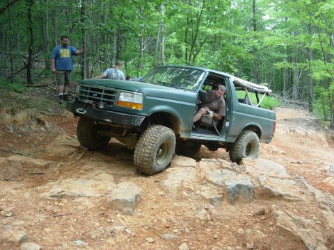 1995 Ford Bronco - Green 1995 Ford Bronco tackling a challenging rocky path during an off-road excursion.