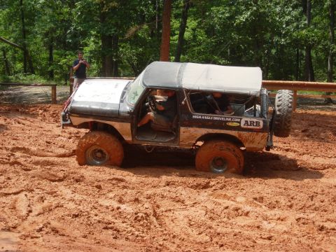 1995 Ford Bronco - Off-road Bronco with soft top is stuck deep in mud, showing signs of off-road use.