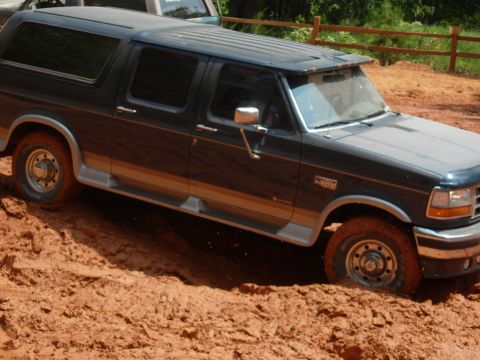 1995 Ford Bronco - A Ford Bronco navigates a muddy trail, with another vehicle in the background.