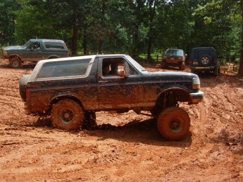 1995 Ford Bronco - Several muddy off-road vehicles navigate a challenging dirt track during an outdoor event.