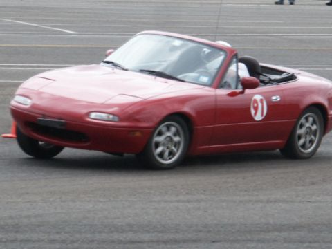 2001 Mercury Grand Marquis - Red Mazda Miata convertible with racing number 91 on the door is seen on a paved surface.