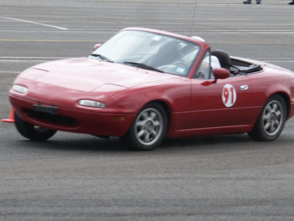 Red Mazda Miata convertible with racing number 91 on the door, on a paved surface