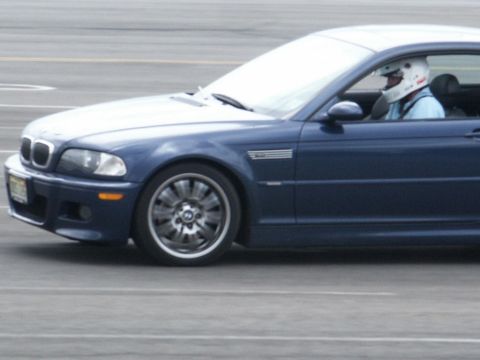 2001 Mercury Grand Marquis - A blue coupe with a driver wearing a racing helmet is seen from the side on a paved surface.