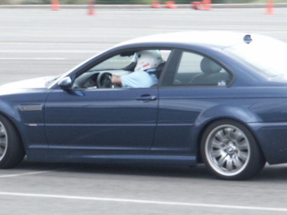 Blue coupe on track, driver wearing helmet. Appears to be a BMW M3