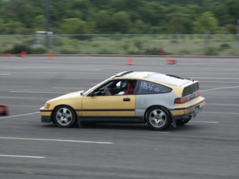 2001 Mercury Grand Marquis - A two-tone Honda CRX, yellow in the front and grey in the rear, is captured in motion on a race track, displaying the number 134G.