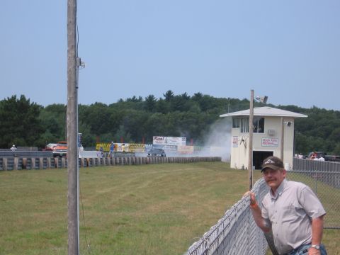 1989 Ford Mustang - Man watches cars at a drag strip, with a control tower and trees in the background.