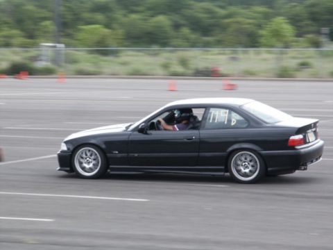 2001 Mercury Grand Marquis - A black BMW E36 coupe is seen in profile on a race track, with orange cones visible in the background.