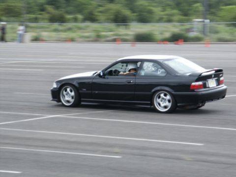 2001 Mercury Grand Marquis - A black coupe with racing numbers on the window is captured in motion on a paved track.