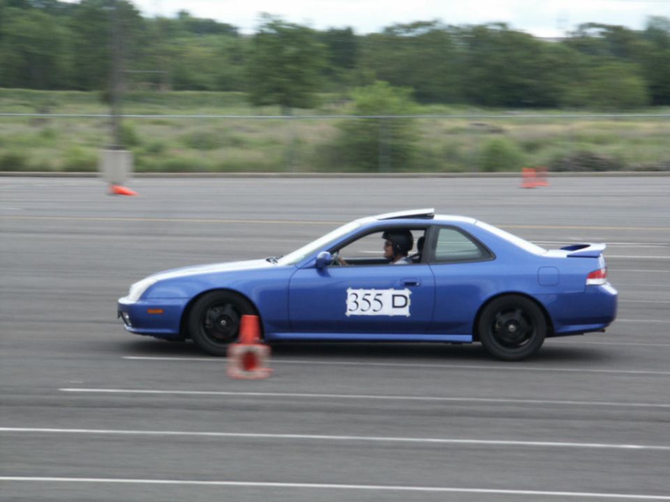 Blue coupe with a racing number '355 D' on the door, driving on a track with orange cones