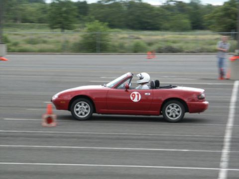 2001 Mercury Grand Marquis - A red convertible sports car with the number 91 on its door navigates a race track, with a driver in a helmet visible.