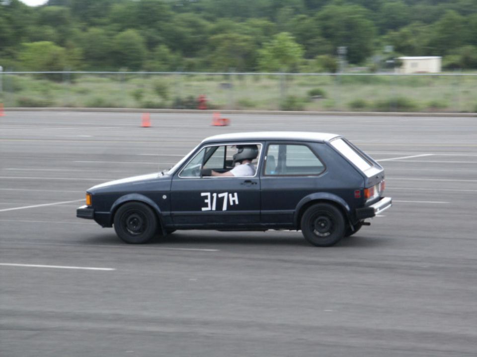 Dark blue hatchback car with racing number 317H on the side, driver wearing a helmet, on a paved track