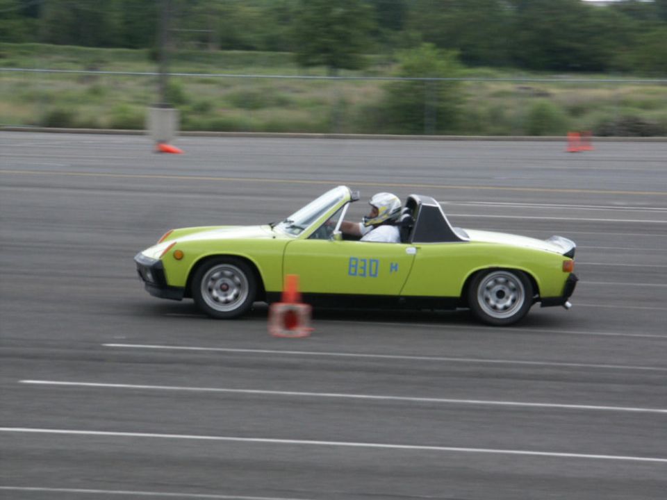 Lime green convertible sports car with number 830 H on the door, driver wearing a helmet, on a track with orange cones