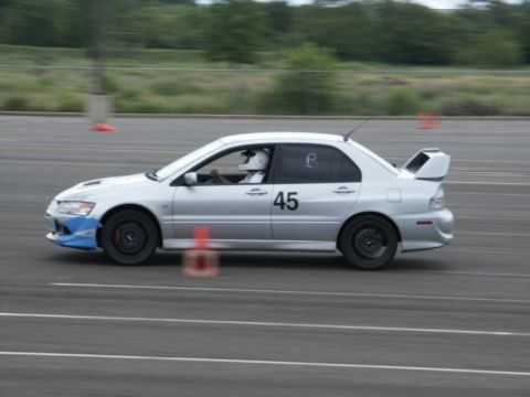 2001 Mercury Grand Marquis - A silver sedan with racing decals and a driver in a helmet navigates a track with orange cones.