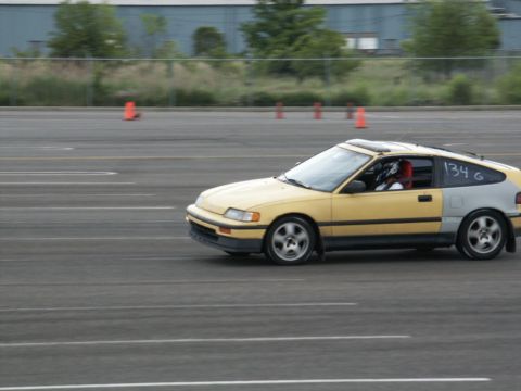 2001 Mercury Grand Marquis - A yellow Honda CRX with a driver wearing a helmet is seen on a paved track with orange cones in the background.