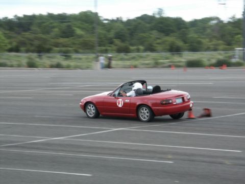 2001 Mercury Grand Marquis - A red convertible sports car navigates a course marked by orange cones, with a driver wearing a helmet.