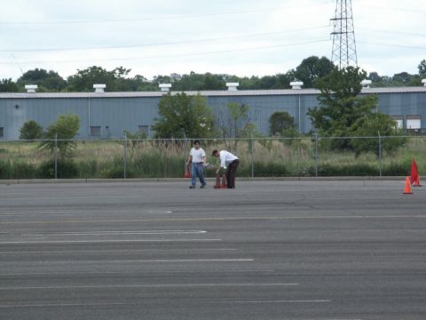 2001 Mercury Grand Marquis - Men arrange traffic cones in a large, empty asphalt lot with a fence and building behind them.