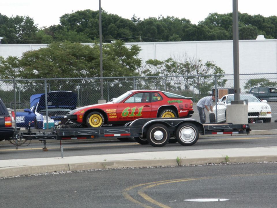 Red race car with number 611 on trailer, being worked on by a person. Another white car is nearby