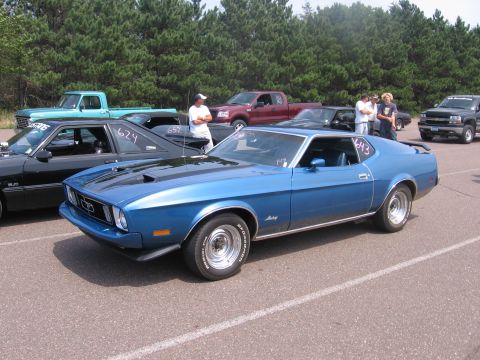 1989 Ford Mustang - A blue 1971 Ford Mustang coupe is parked at a car event, with other vehicles and spectators in the background.