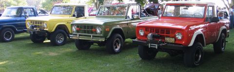 1994 Ford Bronco - Several Ford Broncos are parked on a grassy field, with a red one in the foreground.