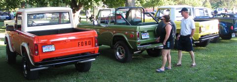 1994 Ford Bronco - Two Ford Broncos, one orange and one green, are parked side-by-side on a grassy lawn at a car show.