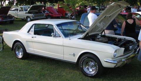 1994 Ford Bronco - A white 1965 Ford Mustang coupe is displayed with its hood open at a car show.
