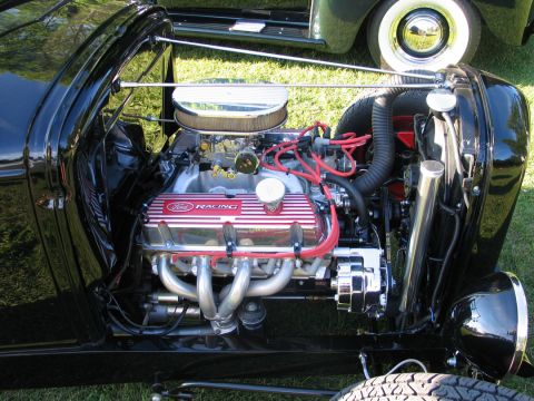 1994 Ford Bronco - Close-up of a black hot rod's engine bay, Ford Racing valve covers and a chrome air cleaner, with another vehicle visible in the background.