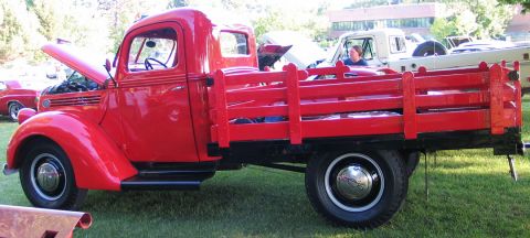 1994 Ford Bronco - A vintage red flatbed truck is displayed outdoors with its hood open, alongside other vehicles.