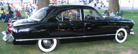 1994 Ford Bronco - Side view of a vintage black sedan with whitewall tires at an outdoor event.