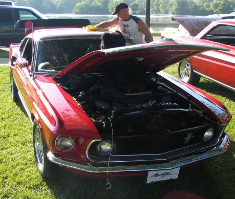 1994 Ford Bronco - A red 1969 Ford Mustang is displayed with its hood open, revealing the engine bay, at an outdoor car show.