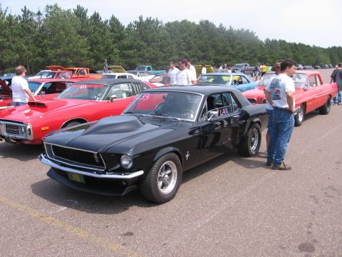 1989 Ford Mustang - A line of classic cars, including a black 1967 Ford Mustang, are parked at an outdoor event.