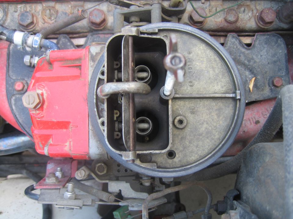 Top-down view into open two-barrel carburetor throat on red intake manifold, air cleaner removed