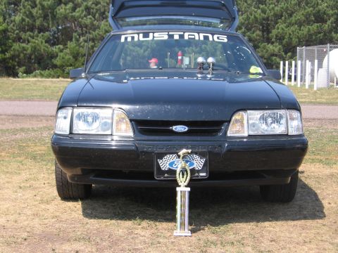 1989 Ford Mustang - A black Ford Mustang is shown from the front with its trunk open and a trophy displayed.