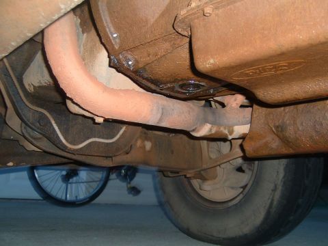 1995 Ford Bronco - The underside of a vehicle, focusing on the exhaust system and transmission, with a bicycle wheel visible below.