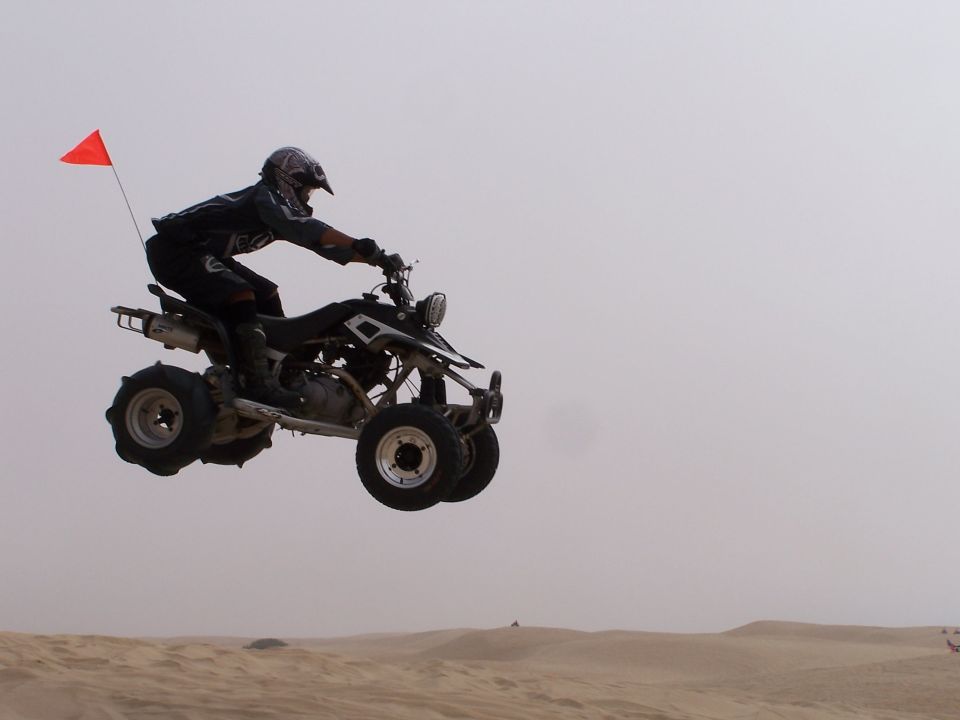 Quad bike with rider jumping over sand dunes, orange flag on back