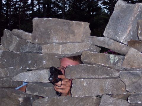 2001 Ford Crown Victoria - A person is hidden behind a stone wall, holding a handgun and looking through a gap.